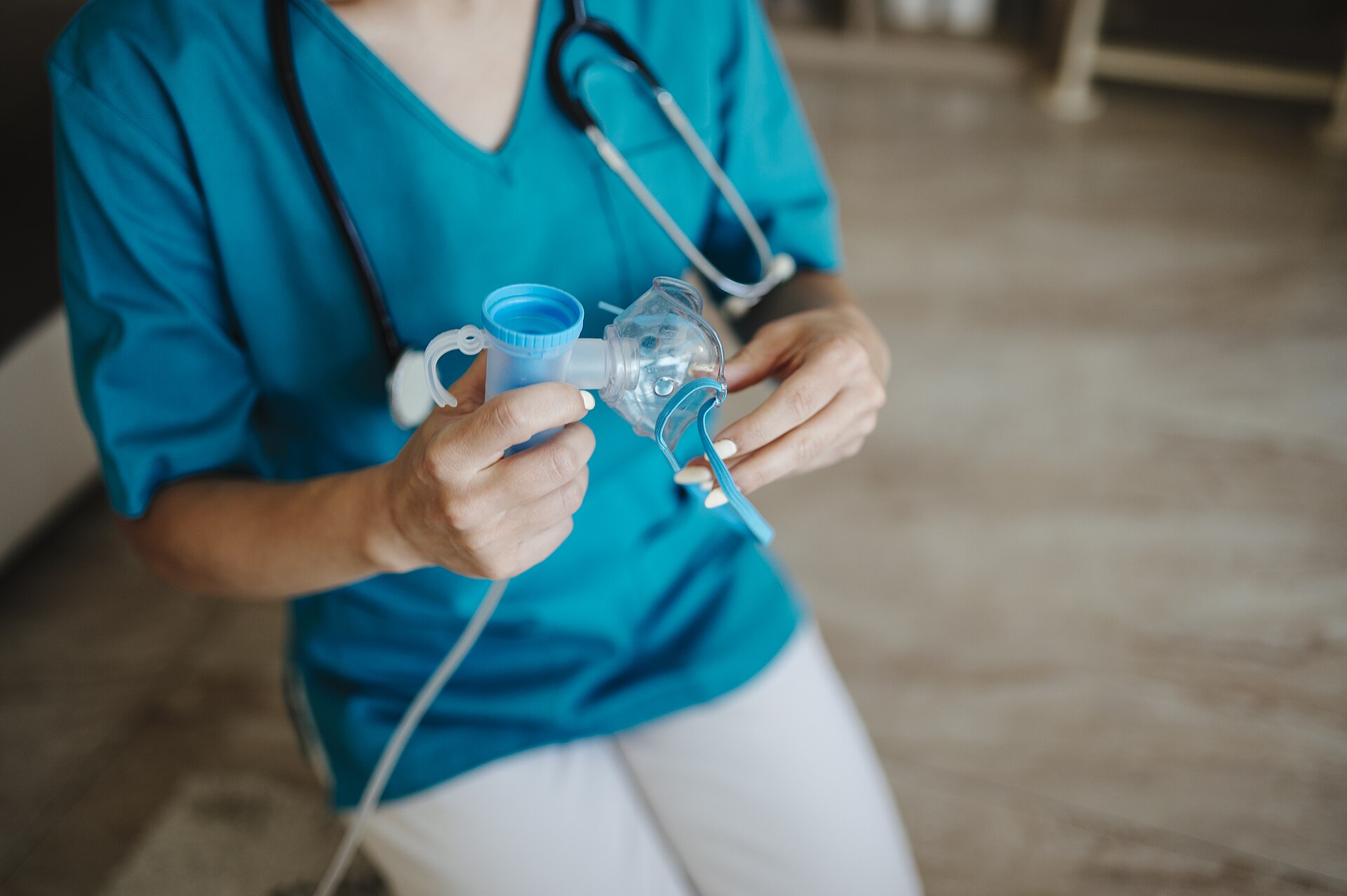 Clinician in teal scrubs with a stethoscope holding a nebulizer mask and medication cup