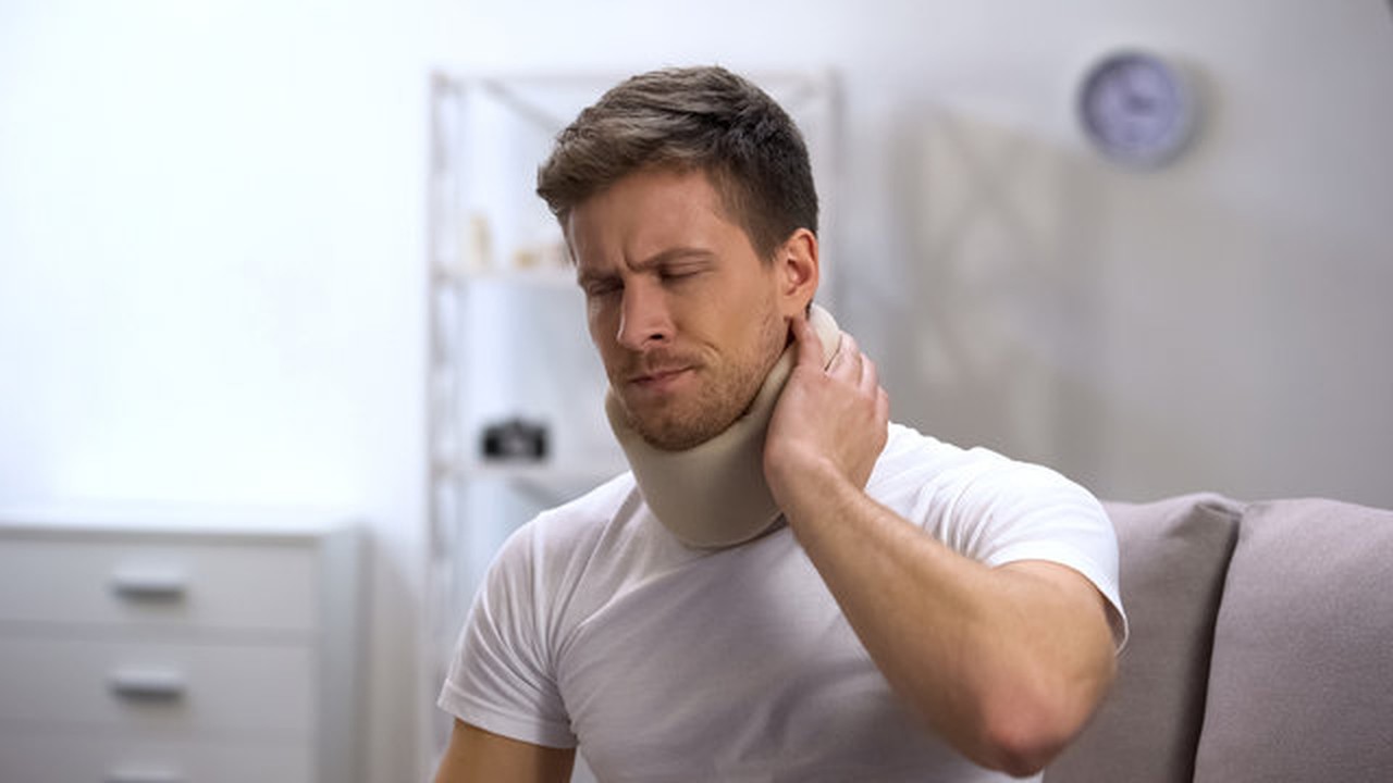 Patient wearing a foam cervical neck brace and holding the back of the neck